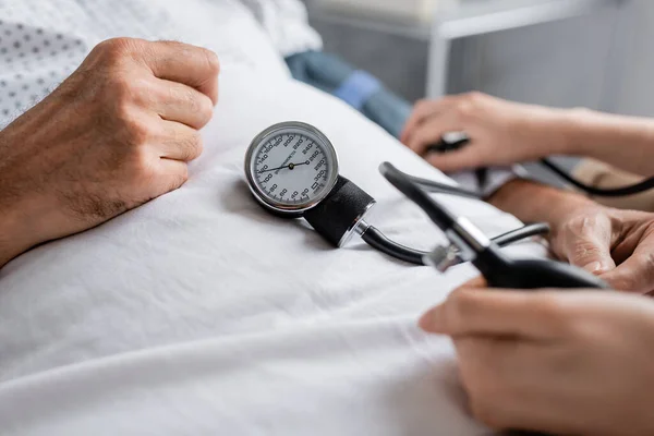 Ausgeschnittene Ansicht des Arztes mit Tonometer, das den Blutdruck eines älteren Patienten auf dem Krankenhausbett überprüft — Stockfoto