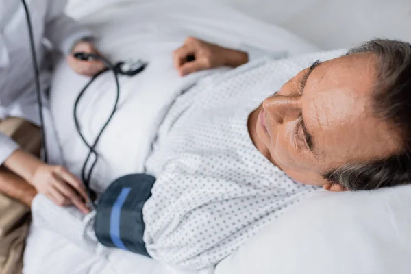 Kranker Patient liegt mit Tonometer neben verschwommenem Arzt in Klinik — Stockfoto