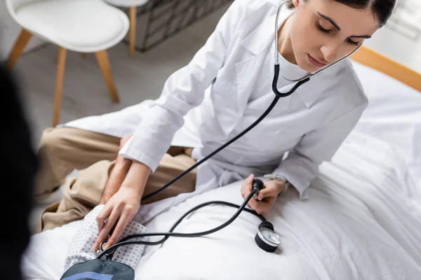 High angle view of doctor checking blood pressure of elderly patient on bed in hospital — Stock Photo