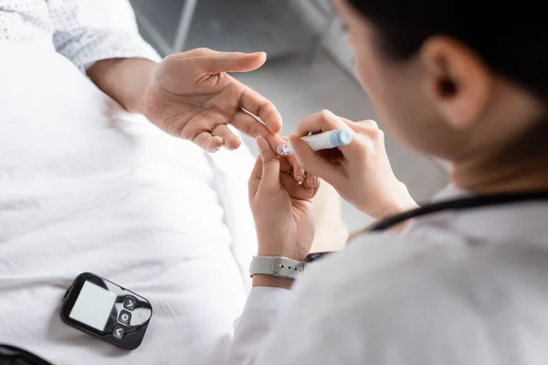 Verschwommener Arzt hält Lanzenstift in der Nähe der Hand eines Diabetes-Patienten auf Krankenhausstation — Stockfoto