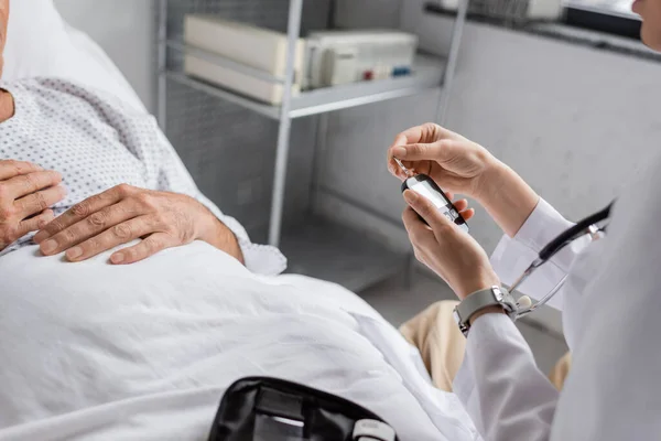 Cropped view of doctor holding glucometer near elderly patient in clinic — Stock Photo