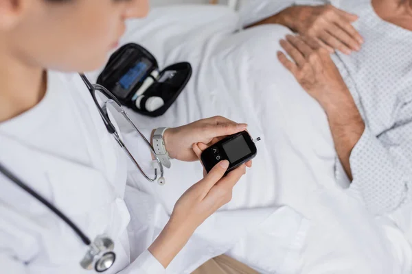 Cropped view of doctor holding glucometer near sick senior patient in hospital — Stock Photo