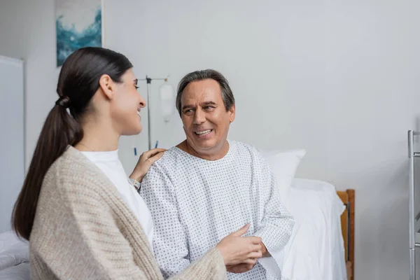 Cheerful patient in gown touching hand of daughter in hospital — Stock Photo