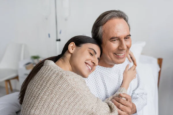Улыбающаяся женщина обнимает отца в больничном халате — стоковое фото