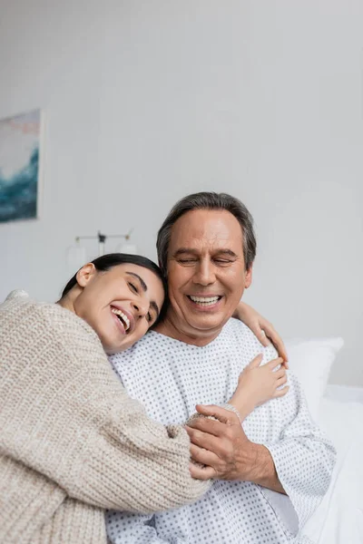Positive daughter hugging father in patient gown in hospital ward — Stock Photo
