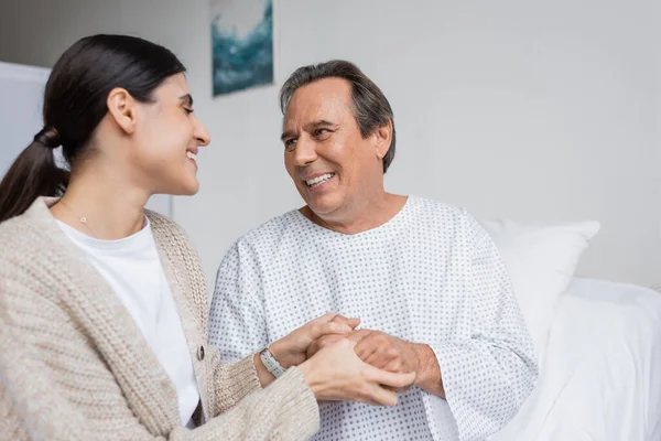 Mulher sorridente segurando a mão do pai na enfermaria do hospital — Fotografia de Stock