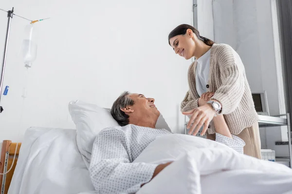 Улыбающийся пожилой мужчина в больничном халате держит за руку дочь в клинике — стоковое фото