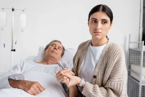 Sad woman holding hand of sick father in hospital ward — Stock Photo