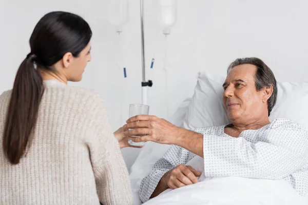 Figlia offuscata che dà un bicchiere d'acqua al padre anziano sul letto d'ospedale — Foto stock
