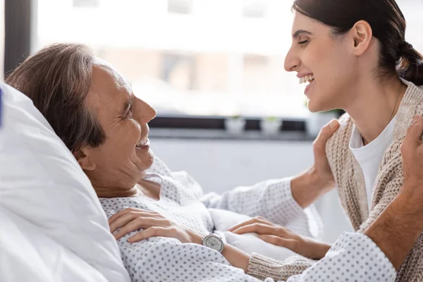 Side view of cheerful woman hugging father in patient gown in hospital — Stock Photo