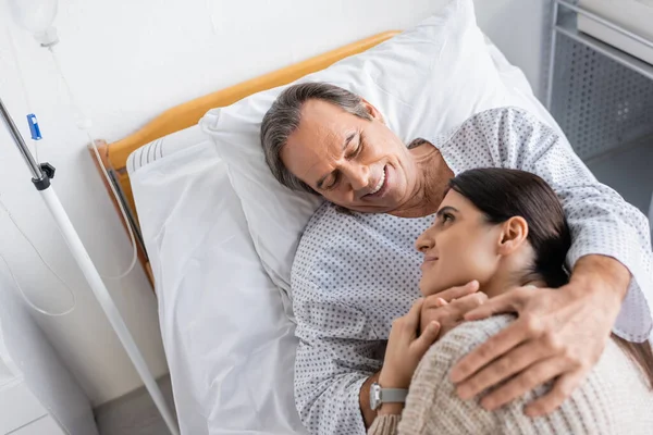 Vista dall'alto del paziente anziano allegro che abbraccia la figlia nel reparto ospedaliero — Foto stock
