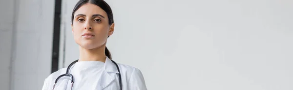 Female doctor in white coat looking at camera in hospital, banner — Photo de stock