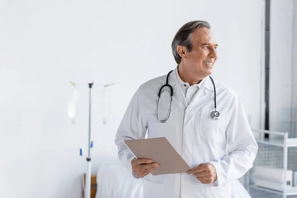 Пожилой врач с бумажной папкой и улыбкой в больничном отделении — стоковое фото