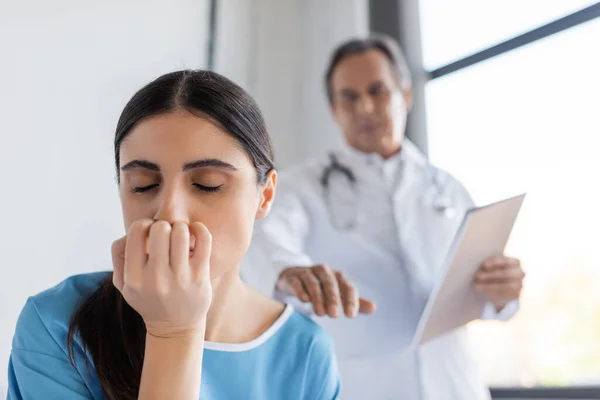 Paziente insoddisfatto che chiude gli occhi vicino a un medico offuscato nel reparto ospedaliero — Foto stock