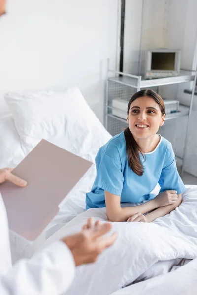 Smiling patient looking at doctor with paper folder in clinic — Stock Photo