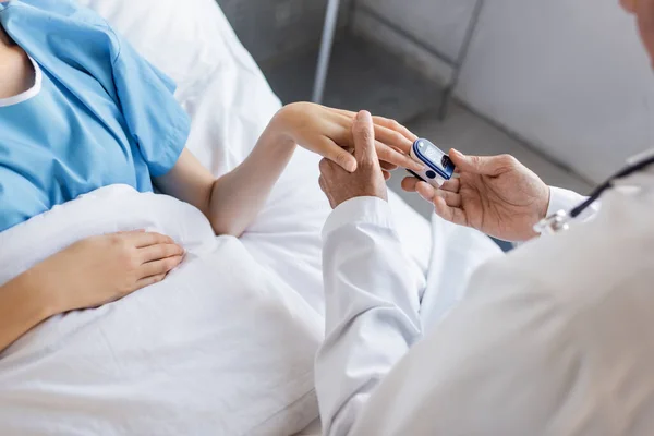 Ausgeschnittene Ansicht eines leitenden Arztes mit Pulsoximeter an der Hand eines Patienten in der Klinik — Stockfoto