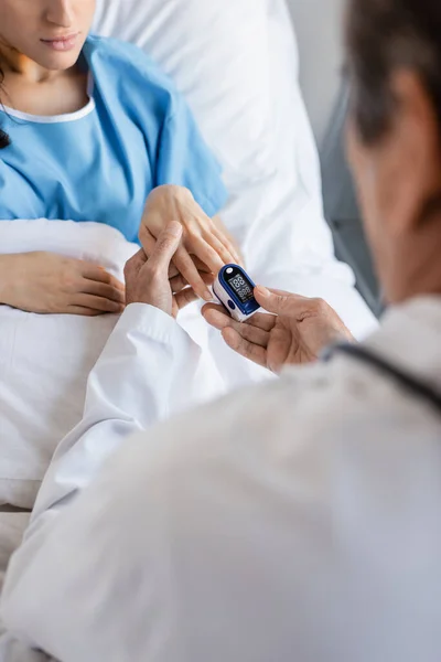 Blurred doctor wearing pulse oximeter on finger of patient in hospital - foto de stock