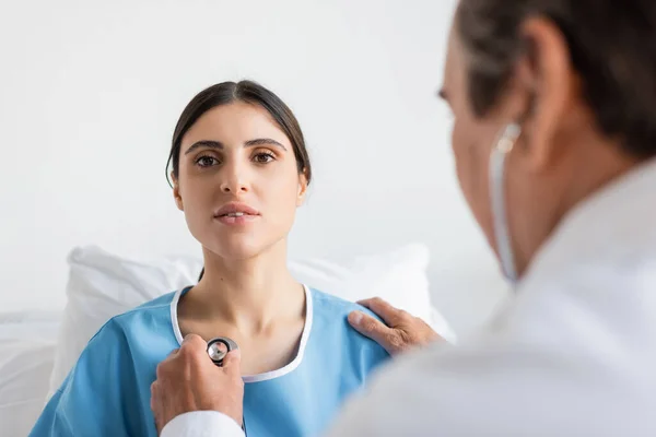 Blurred doctor holding stethoscope near chest of patient in clinic — Stock Photo