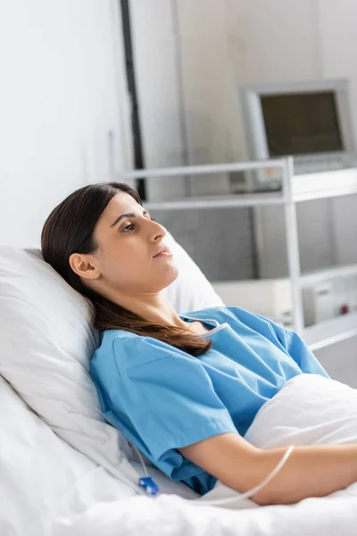 Больной пациент в халате лежит рядом с внутривенной терапией в клинике — стоковое фото