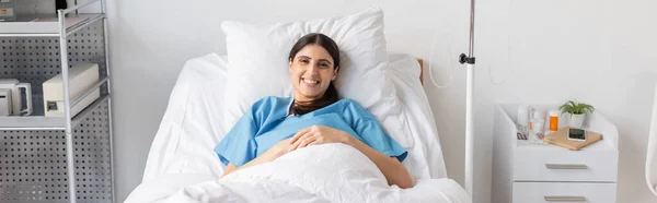 Positive patient smiling at camera on bed in hospital ward, banner — Stock Photo