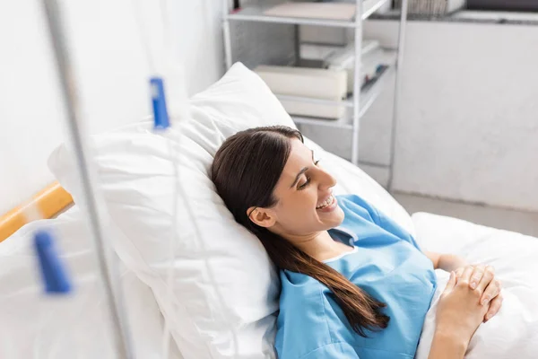 Mulher sorridente deitada perto de terapia intravenosa na clínica — Fotografia de Stock