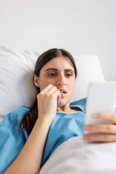 Stressed patient using smartphone while lying on bed in hospital ward — Stock Photo