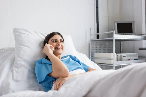 Positiver Patient spricht auf dem Smartphone, während er in der Klinik im Bett liegt — Stockfoto