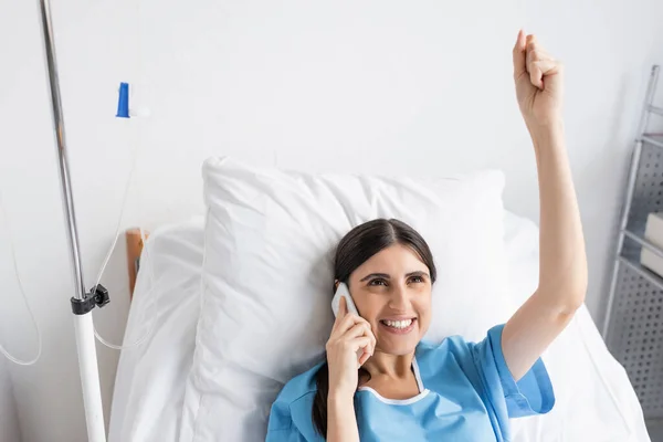 Высокий угол обзора взволнованного пациента, разговаривающего на смартфоне на кровати в больнице — стоковое фото
