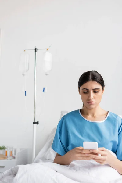 Paziente bruna che usa il cellulare mentre è seduto sul letto in ospedale — Foto stock