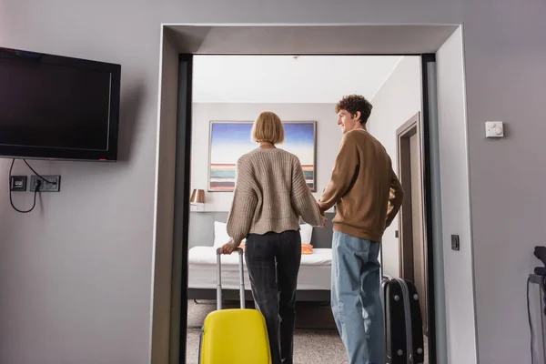 Вид ззаду молодих туристів з валізами, що тримаються за руки в сучасному готельному номері — стокове фото