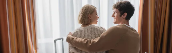 Back view of brunette man hugging happy blonde girlfriend in hotel apartments, banner — Fotografia de Stock