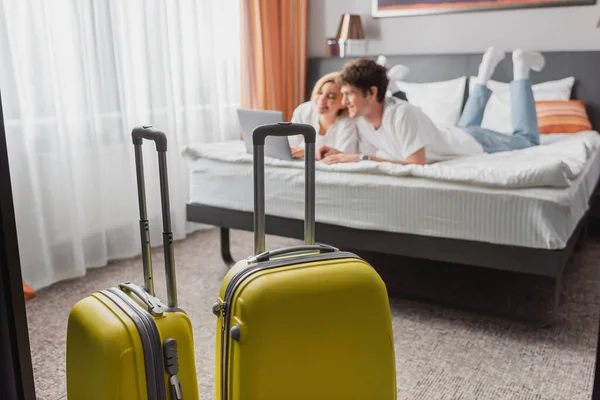 Селективный фокус чемоданов возле молодых путешественников, смотрящих кино на ноутбуке в современной спальне отеля — стоковое фото