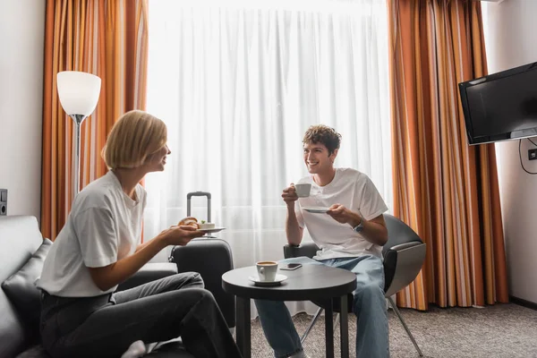 Happy young couple looking at each other while having breakfast in modern hotel suite — Fotografia de Stock