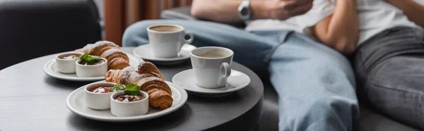 Tasty croissants with jam and chocolate paste near coffee cups and cropped couple on blurred background, banner — Stock Photo