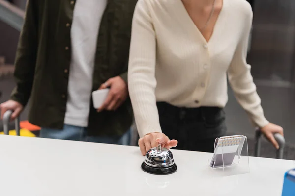 Partial view of woman ringing service bell on reception near blurred boyfriend with smartphone in hotel — Stockfoto