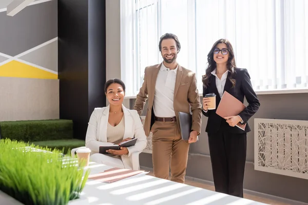Happy multiethnic business people smiling at camera near desk in modern office — Fotografia de Stock