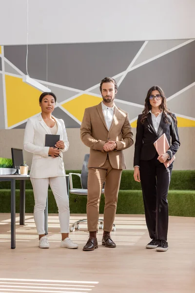 Full length of multicultural business people looking at camera while standing in modern office — Stock Photo