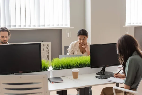 Concentrated multiethnic business people working near monitors with blank screen in modern office — Stock Photo