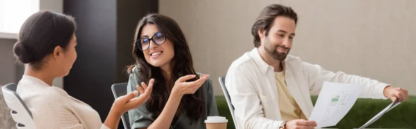 Young manager looking at blueprint while multiethnic businesswomen talking in office, banner — Stock Photo