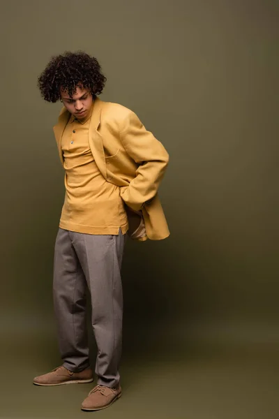 Full length of african american man in yellow blazer and trousers posing with hand behind back on grey green background — Stock Photo