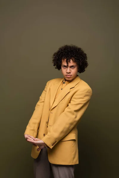 Trendy african american man in yellow blazer looking at camera while posing with clenched hands on olive grey background — Stock Photo