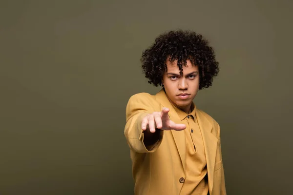 Young and curly african american man in yellow jacket pointing with finger at camera isolated on grey — Stock Photo
