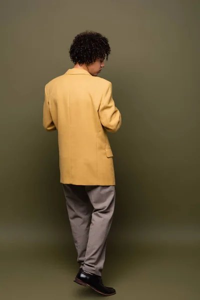 Back view of young african american man in yellow blazer and trousers on grey green background — Stock Photo