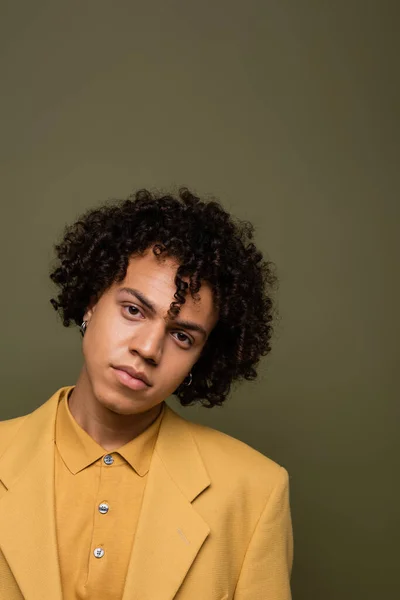 Portrait of curly african american man in yellow jacket and shirt looking at camera on grey green background — Foto stock