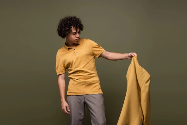 Стильний афроамериканський чоловік в сорочці поло і штани, що тримають жовтий піджак ізольовані на сірому — стокове фото
