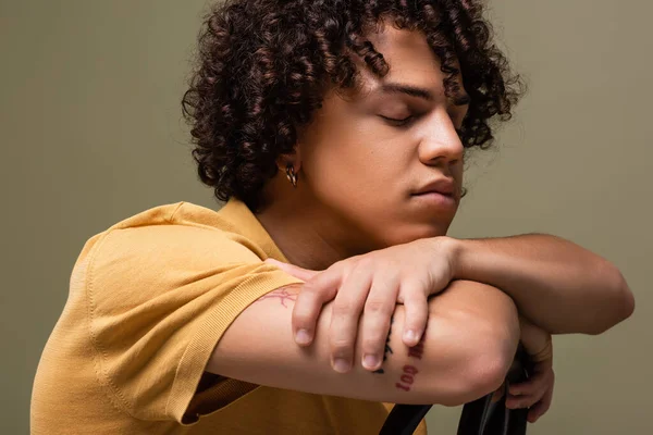 Stylish african american man with closed eyes and wavy hair leaning on chair back isolated on grey — Stock Photo