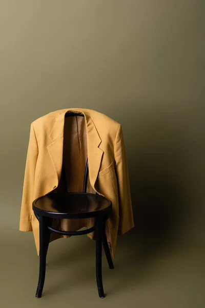 Fashionable yellow blazer hanging on black wooden chair on olive green background — Photo de stock