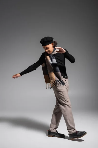 Full length of young and stylish african american man in plaid scarf and beret stepping on grey background — Stock Photo