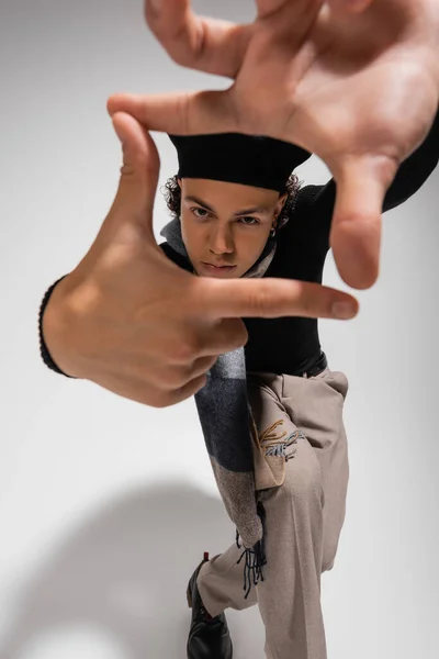 African american man in black beret and pants showing snapshot gesture and looking at camera on grey — Stock Photo