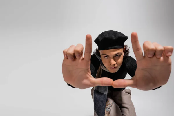 African american man in black beret and warm scarf looking at camera and showing snapshot gesture on grey — Stock Photo